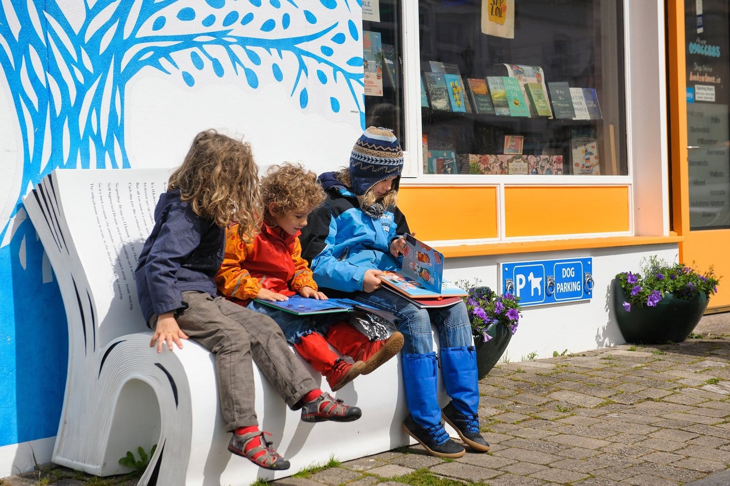 Three children reading outside a community library, thanks to their contributions to us, helping us build a better future with social impact