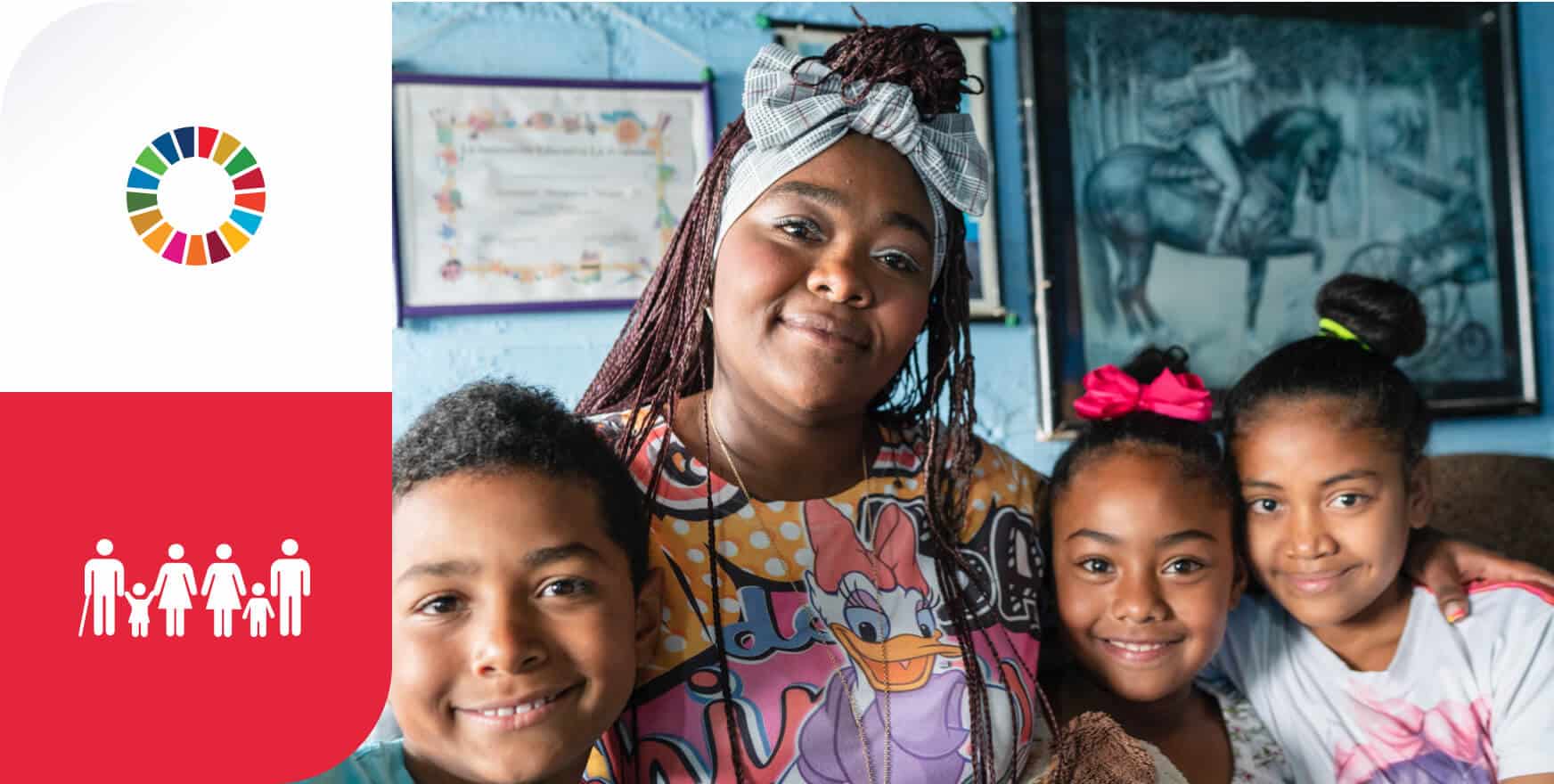 Mujer sonriente rodeada de tres niños, todos con expresiones de felicidad y cercanía, reflejando el compromiso de One Inversión Social con los ODS. La mujer, que lleva una camiseta colorida con un estampado de un personaje de dibujos animados, tiene una diadema de tela en la cabeza y el cabello trenzado. Los niños también están sonrientes, cada uno con un peinado distintivo, y parecen estar en un ambiente acogedor con una pared azul de fondo, decorada con cuadros y certificados enmarcados. A la izquierda de la imagen, hay un diseño gráfico con los colores de los Objetivos de Desarrollo Sostenible (ODS) y un ícono que representa una familia, con un fondo en rojo. Las palabras 